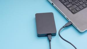 Black external hard disk connecting to a laptop on a blue background.